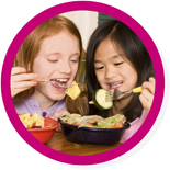 Round photo with a magenta border of two young girls eating salad
