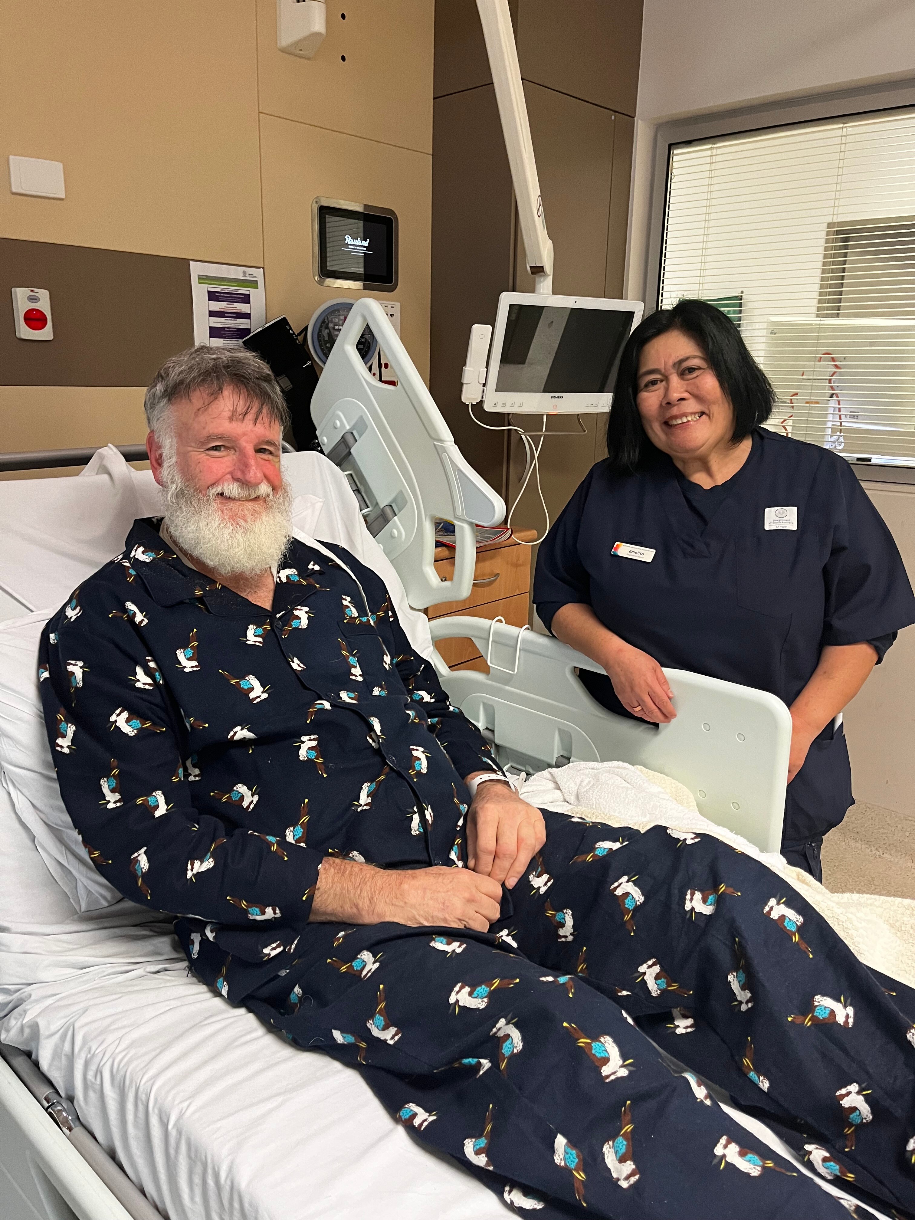 A patient sitting in a hospital bed with a nurse beside the bed in a stroke unit room.