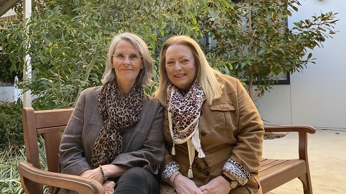 Two females sitting on a bench outside